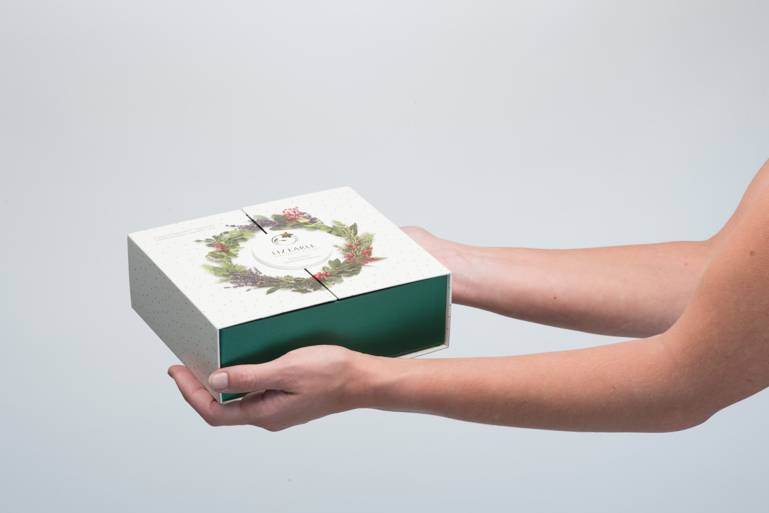 Witte Luxline graphic met stipjes en bloemenkrans voor cosmetische verpakkingen vast in handen • Solidus