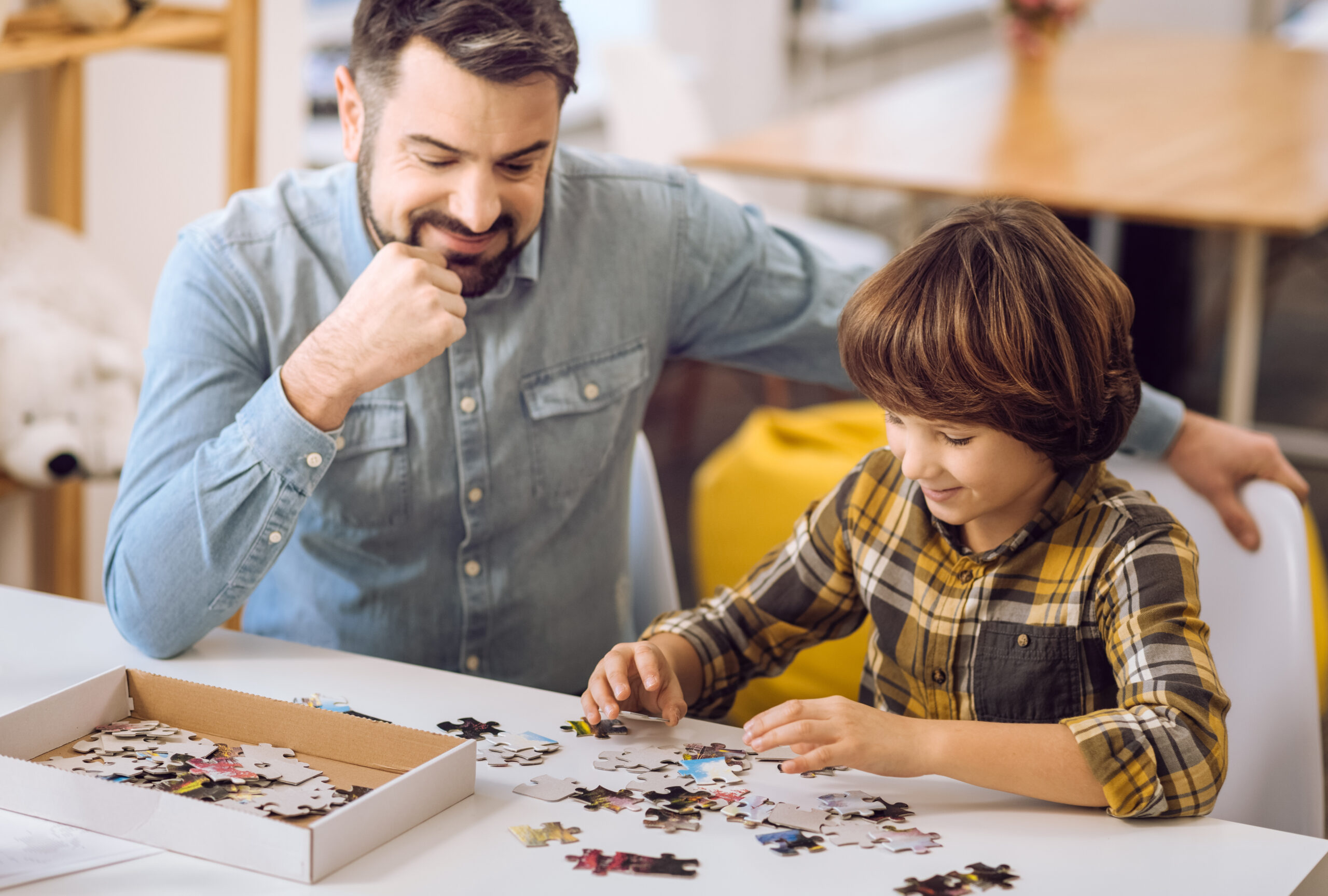 Padre feliz mirando a su hijo jugar con un rompecabezas • Solidus